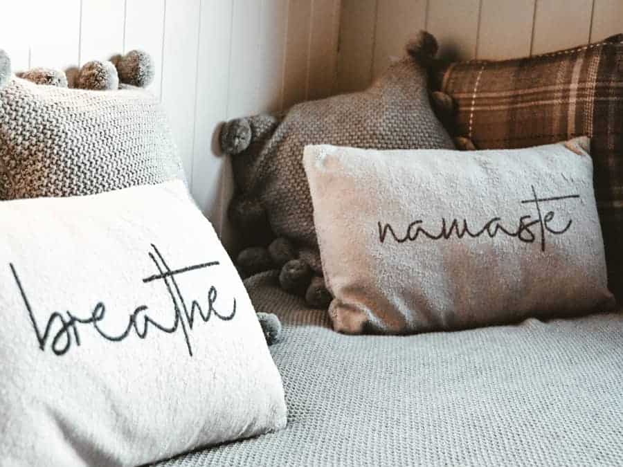 Dekorative Kissen mit den Worten ‚breathe‘ und ‚Namaste‘ auf einem Sofa, als Symbol für die kommerzielle Nutzung spiritueller Begriffe.