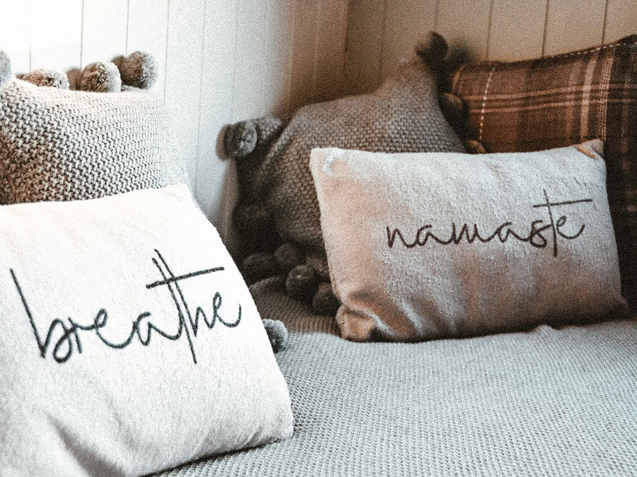 Dekorative Kissen mit den Worten ‚breathe‘ und ‚Namaste‘ auf einem Sofa, als Symbol für die kommerzielle Nutzung spiritueller Begriffe.