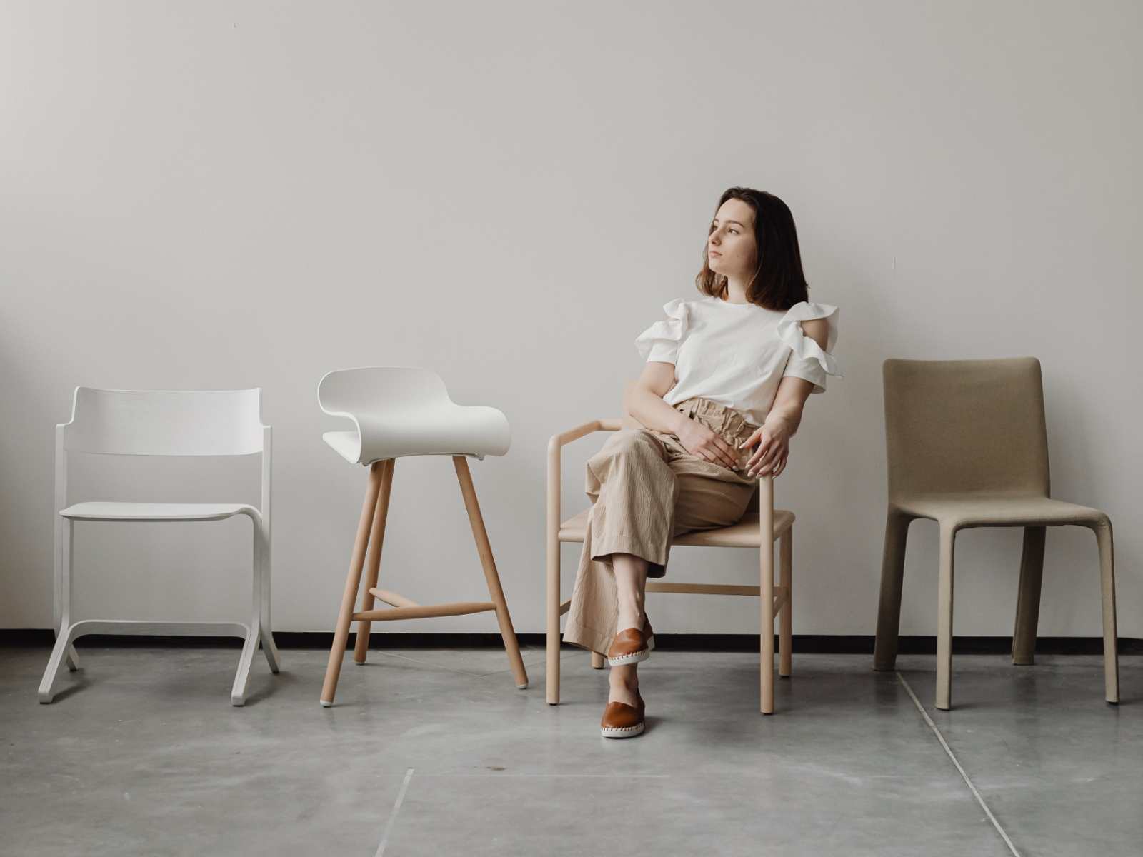 Frau sitzt nachdenklich zwischen verschiedenen Stühlen und überlegt Coaching-Ausbildung und Berufsweg als Coach