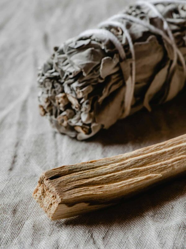 Räuchern mit weißem Salbei und Palo Santo auf hellem Stoffuntergrund