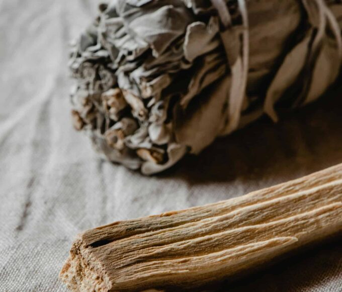 Räuchern mit weißem Salbei und Palo Santo auf hellem Stoffuntergrund