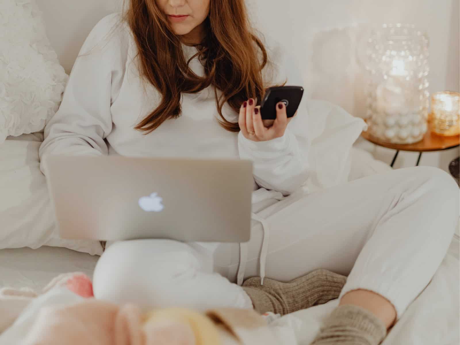 Person sitzt im Bett mit Laptop und Smartphone, Kerzenlicht im Hintergrund – eine Szene, die die Rauhnächte im Spannungsfeld von Rückzug und digitaler Vermarktung zeigt.