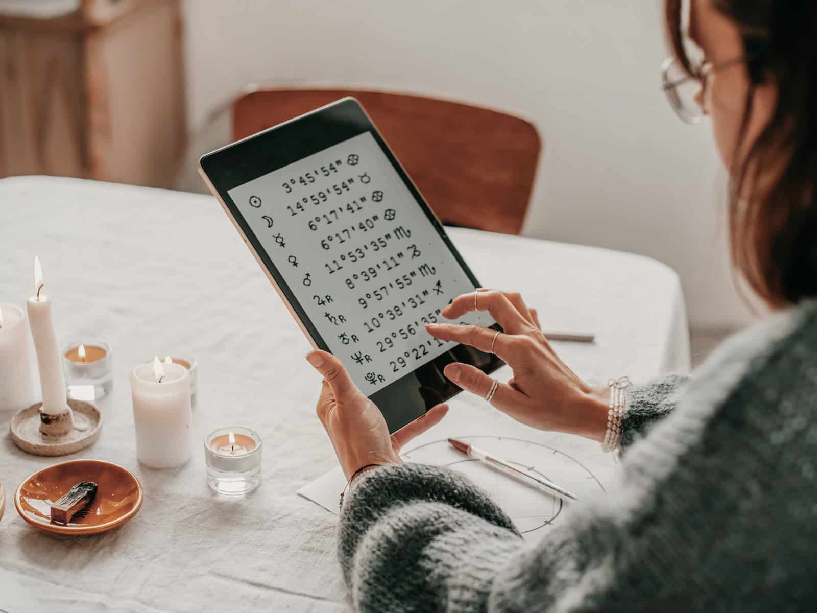 Frau konsultiert astrologische Deutungen auf Tablet mit Planetenpositionen und Symbolen