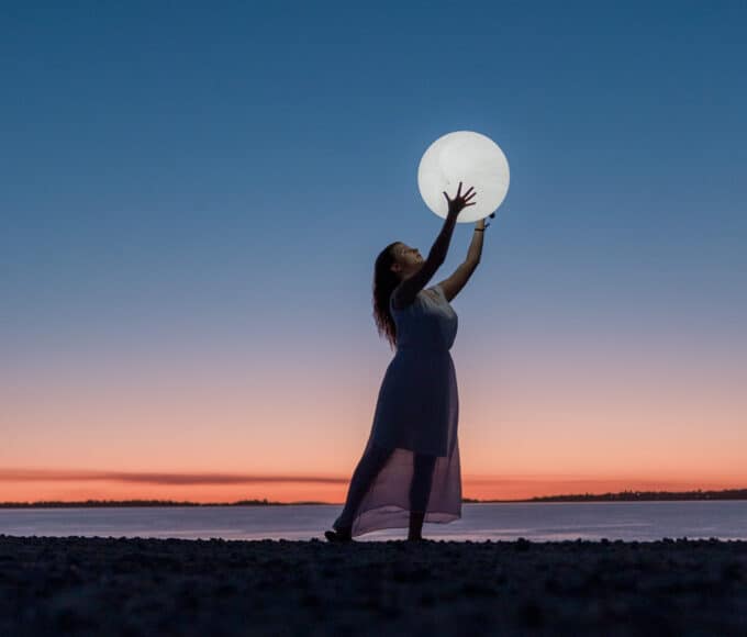 Frau hält leuchtenden Mond am Strand bei Sonnenuntergang – symbolisiert die emotionale Anziehung der Astrologie