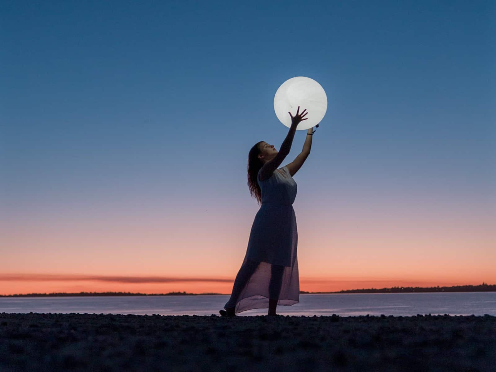 Frau hält leuchtenden Mond am Strand bei Sonnenuntergang – symbolisiert die emotionale Anziehung der Astrologie
