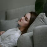 Junge Frau liegt nachdenklich auf einer Couch – Sinnbild für Followerinnen, die Inhalte von Influencerinnen konsumieren