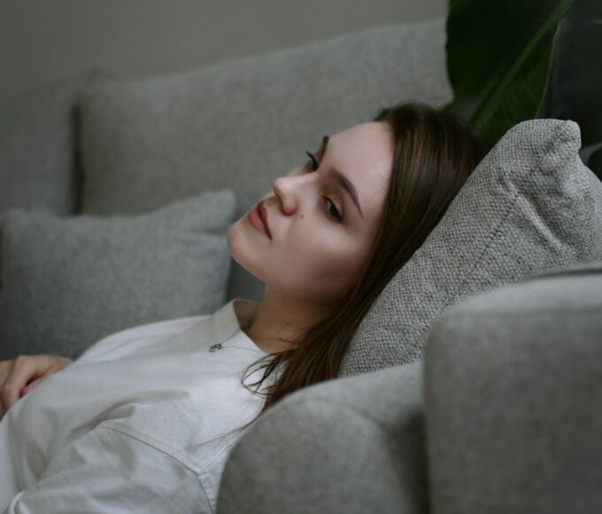 Junge Frau liegt nachdenklich auf einer Couch – Sinnbild für Followerinnen, die Inhalte von Influencerinnen konsumieren