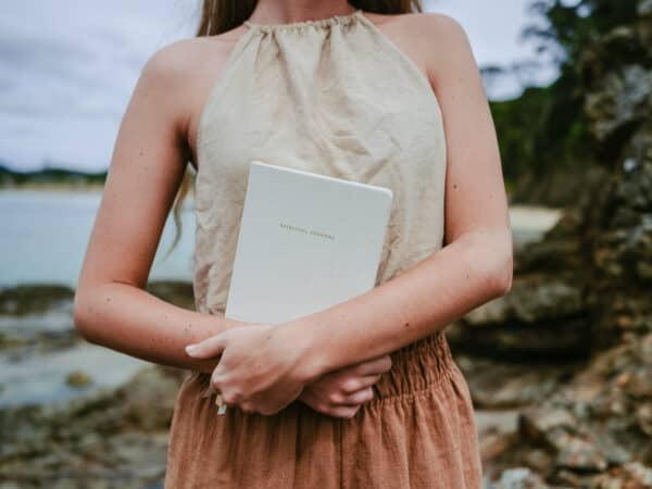 Frau mit Journal im Arm steht an einem Strand