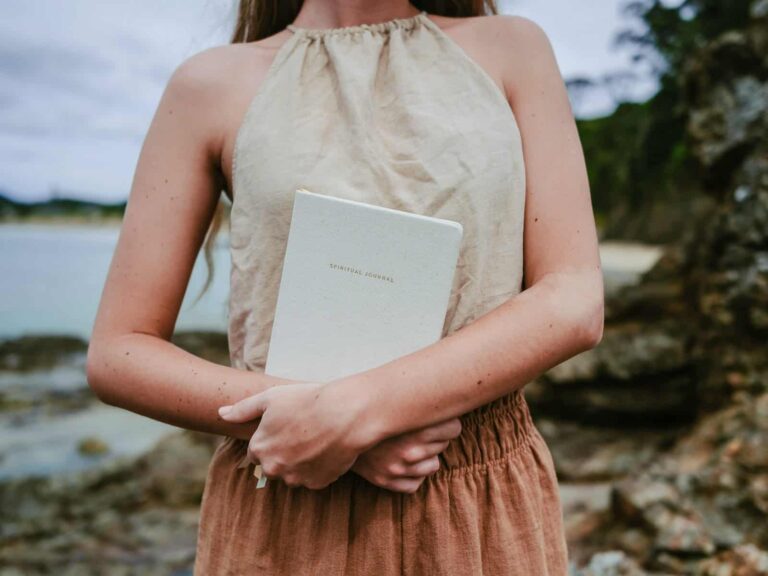 Frau mit Journal im Arm steht an einem Strand