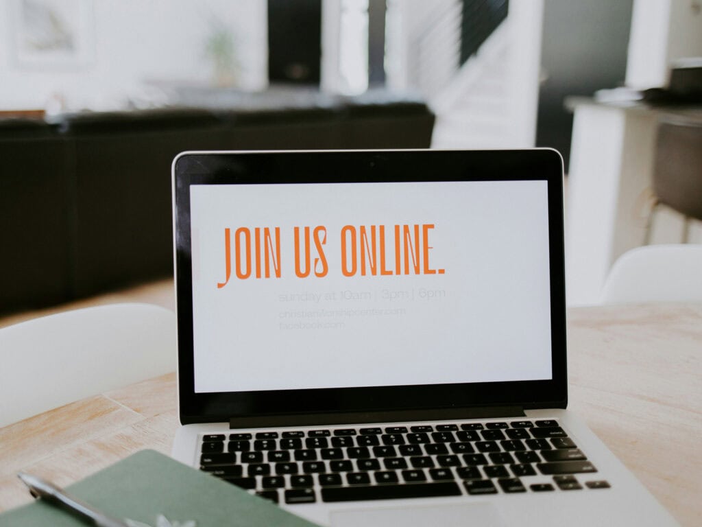 Laptop mit der Aufschrift „Join us online“ auf einem Schreibtisch – Symbol für kommerzielle Spiritualität, die als wissenschaftlich legitimiertes Onlineangebot vermarktet wird.