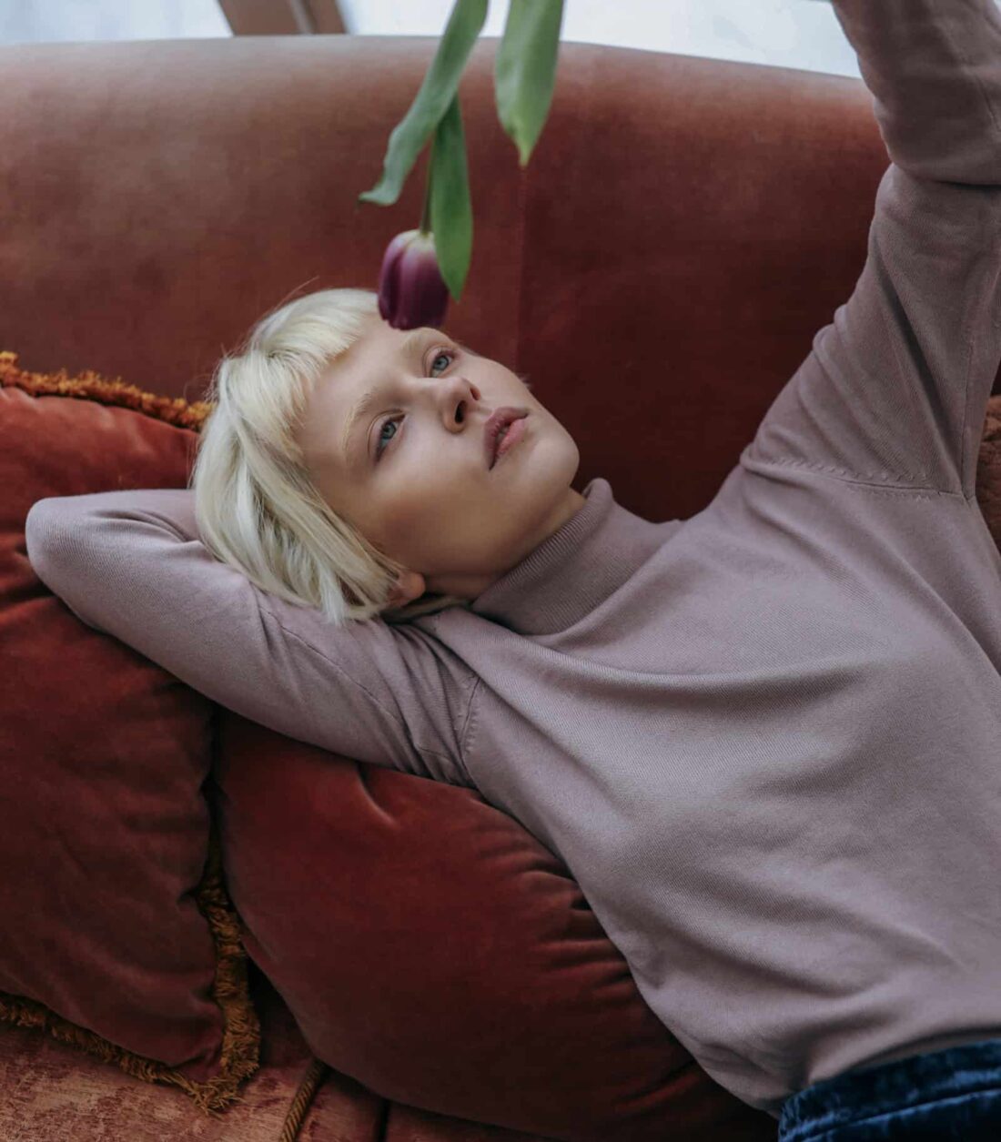 Frau liegt entspannt auf einer Couch und beschäftigt sich passiv mit einem Objekt; Darstellung einer von Influencerinnen geprägten, nach innen gerichteten Lebenshaltung ohne sichtbare Aktivität.