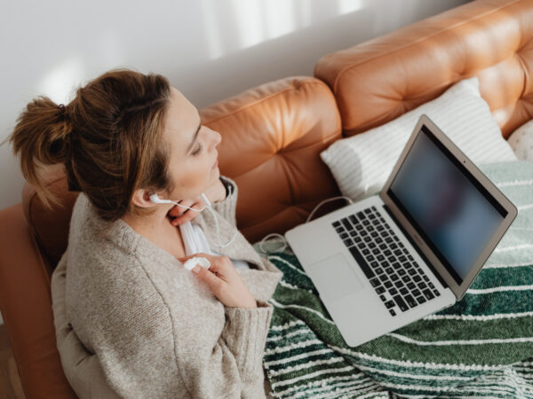 Frau sitzt auf einem Sofa und schaut auf einen Laptop, dessen Bildschirm unscharf ist.