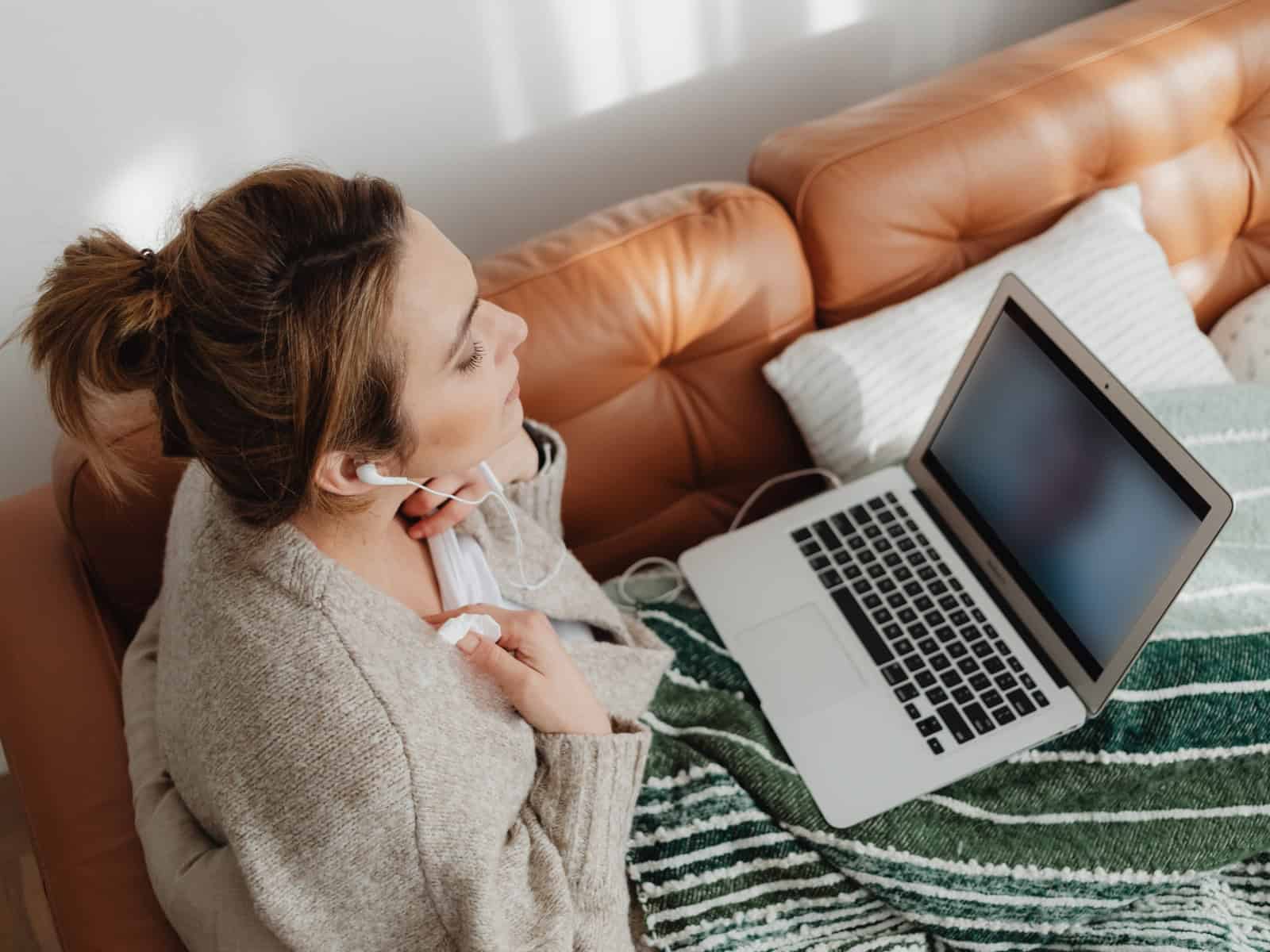Frau sitzt auf einem Sofa und schaut auf einen Laptop, dessen Bildschirm unscharf ist.