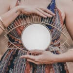 Junge Seelen, alte Seelen – Frau hält einen runden Spiegel vor dem Oberkörper, Hände ruhig im Fokus, natürliche warme Outdoor-Stimmung