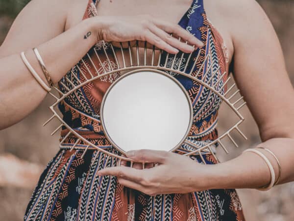 Junge Seelen, alte Seelen – Frau hält einen runden Spiegel vor dem Oberkörper, Hände ruhig im Fokus, natürliche warme Outdoor-Stimmung