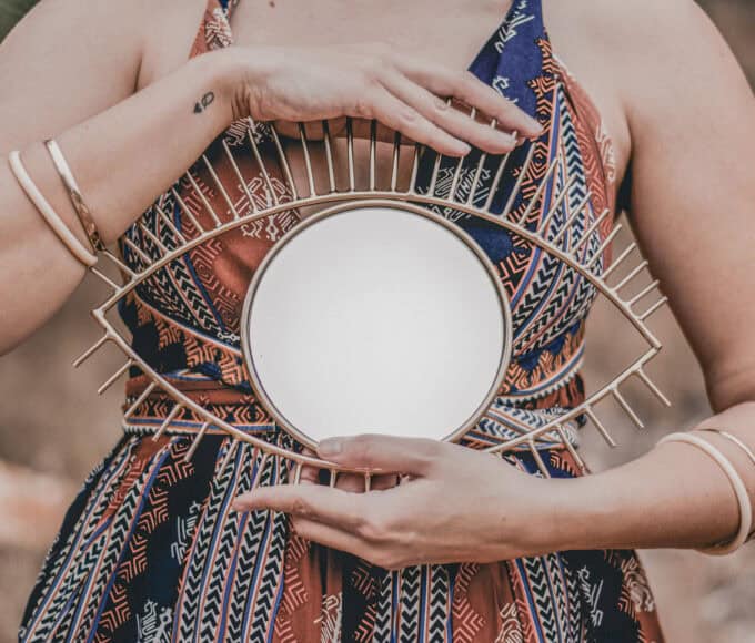 Junge Seelen, alte Seelen – Frau hält einen runden Spiegel vor dem Oberkörper, Hände ruhig im Fokus, natürliche warme Outdoor-Stimmung