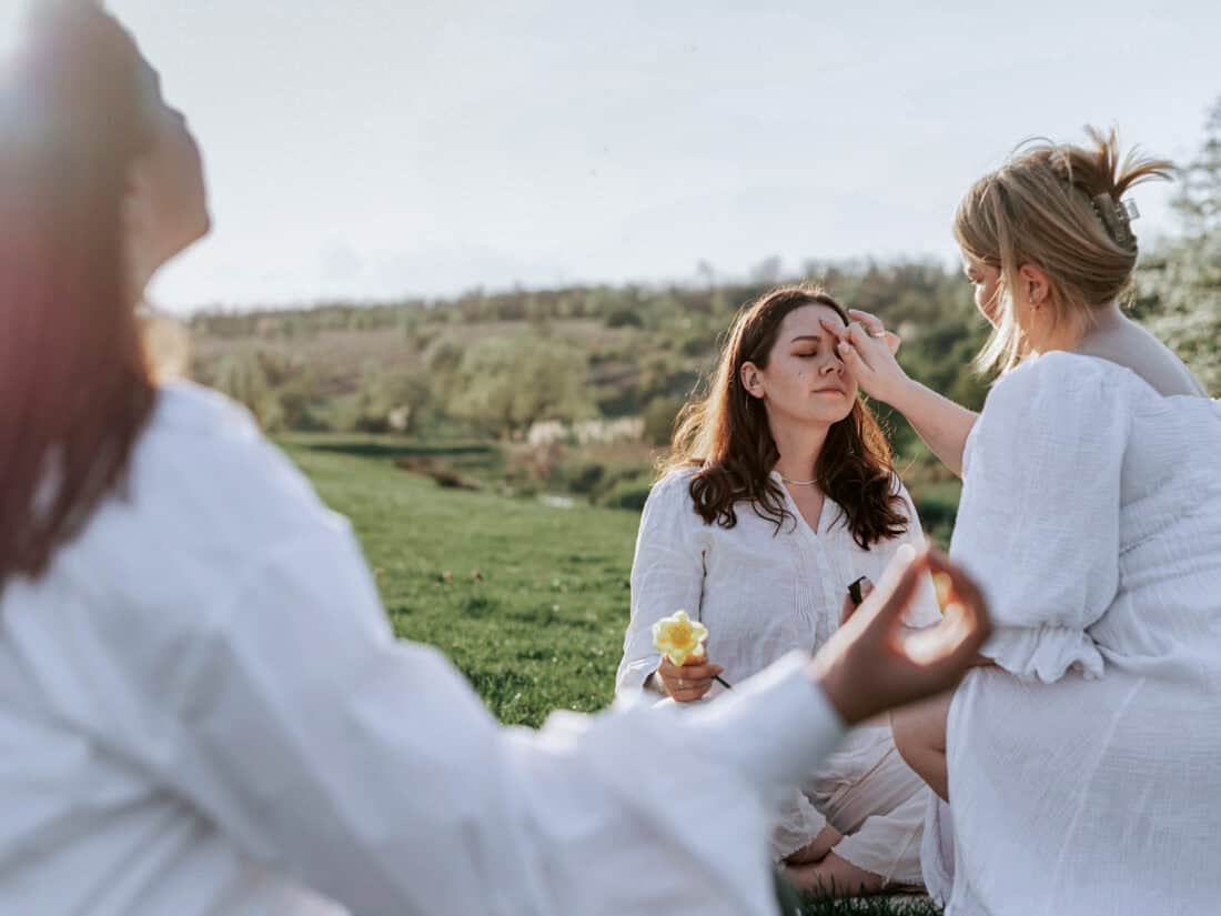Zwei Personen berühren die Stirn einer sitzenden Frau bei einem Ritual, das häufig mit der Aktivierung des „dritten Auges“ und der Zirbeldrüse in Verbindung gebracht wird.