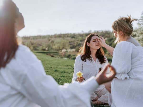 Zwei Personen berühren die Stirn einer sitzenden Frau bei einem Ritual, das häufig mit der Aktivierung des „dritten Auges“ und der Zirbeldrüse in Verbindung gebracht wird.