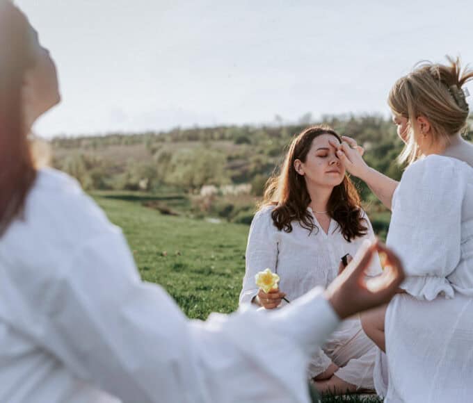 Zwei Personen berühren die Stirn einer sitzenden Frau bei einem Ritual, das häufig mit der Aktivierung des „dritten Auges“ und der Zirbeldrüse in Verbindung gebracht wird.
