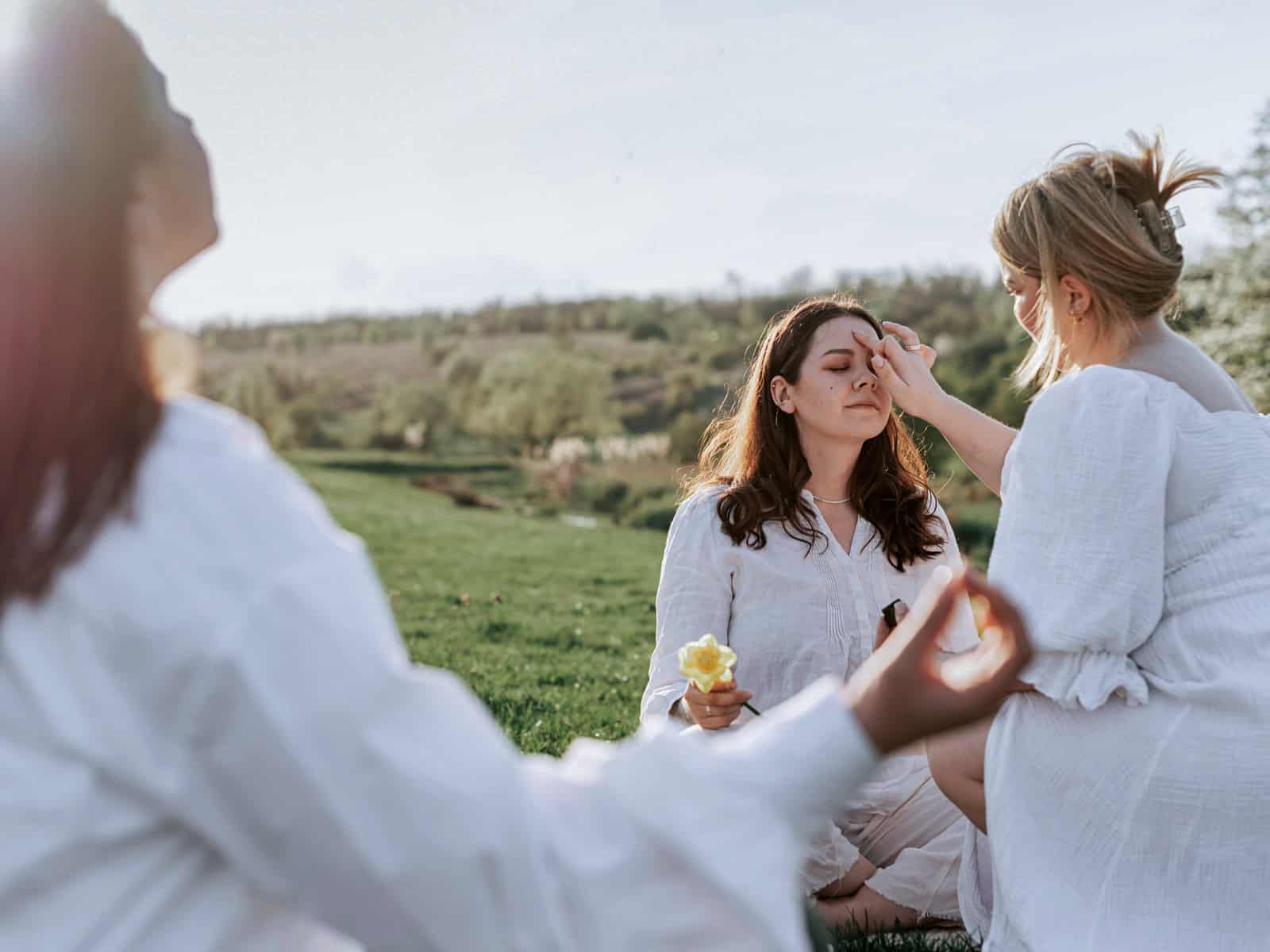Zwei Personen berühren die Stirn einer sitzenden Frau bei einem Ritual, das häufig mit der Aktivierung des „dritten Auges“ und der Zirbeldrüse in Verbindung gebracht wird.
