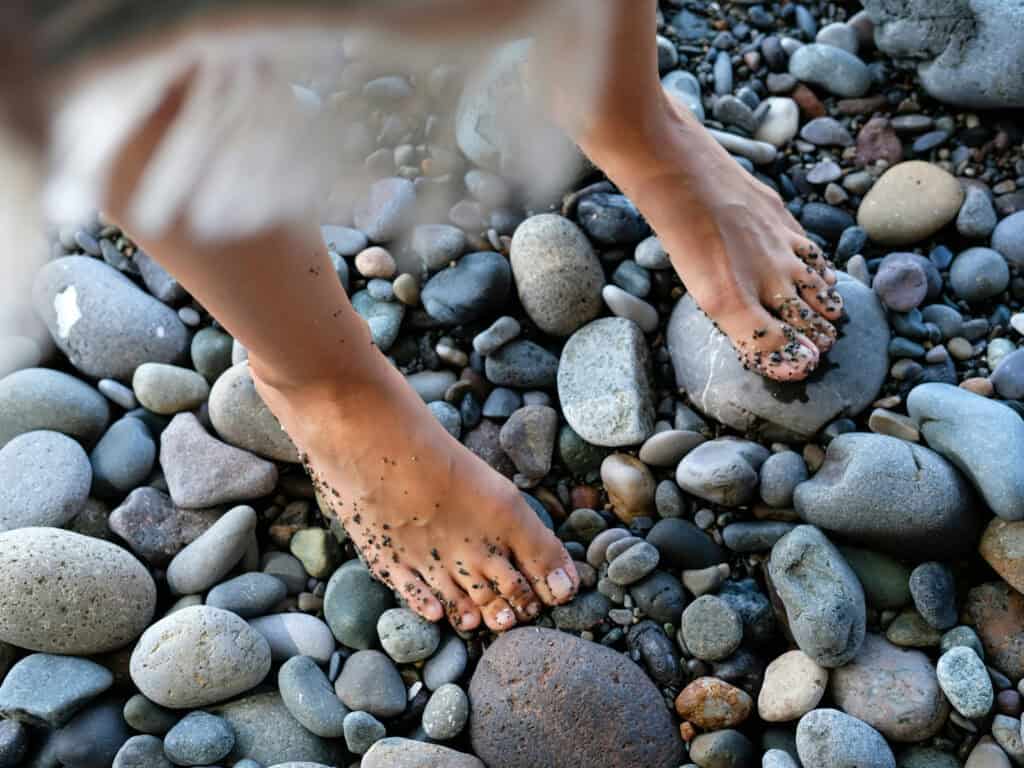 Barfüßige Füße stehen auf Kieselsteinen am Boden.