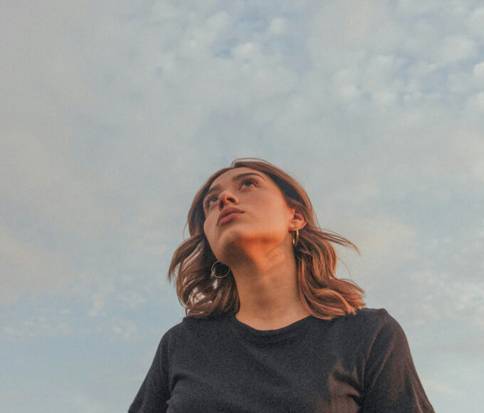 Junge Frau blickt nachdenklich in den Himmel.