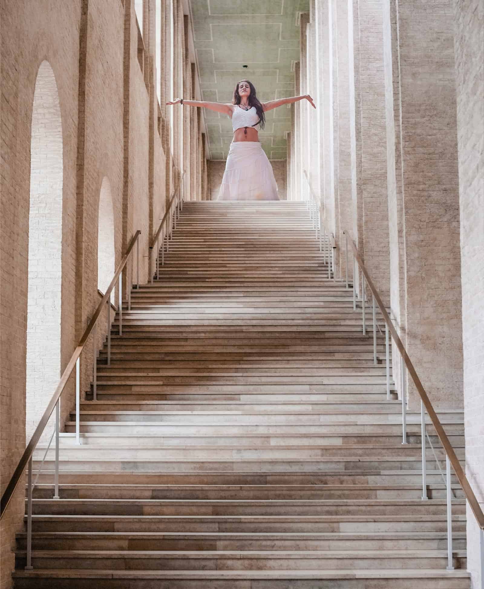Frau in weißer Kleidung steht mit ausgebreiteten Armen am oberen Ende einer großen Treppe – Symbolbild zum Thema „Junge seelen, Alte seelen“ und spirituelle Hierarchien