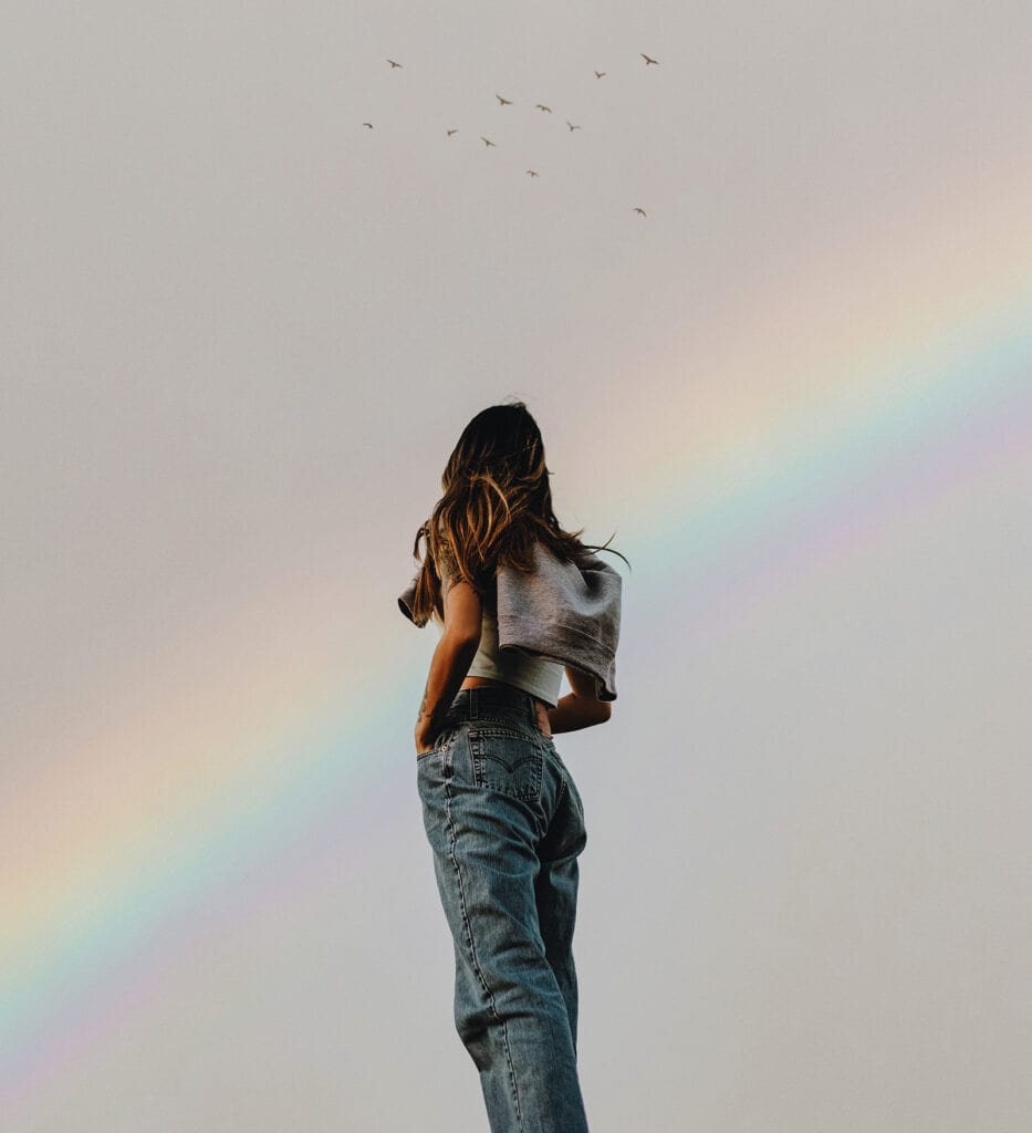 Frau blickt zu einem Regenbogen am Himmel.