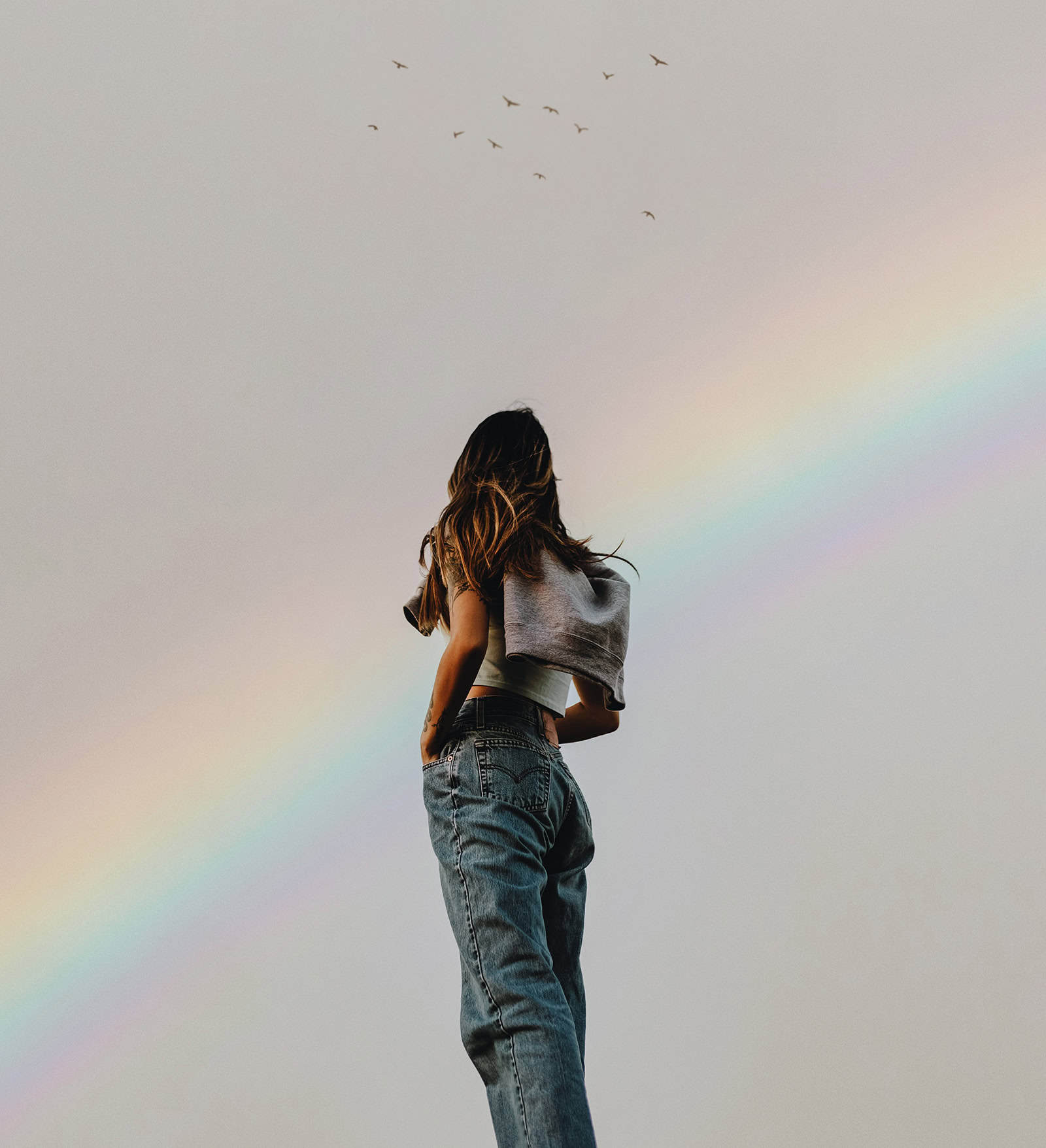 Frau blickt zu einem Regenbogen am Himmel.