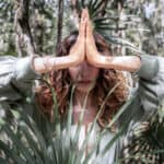 Person im Wald mit gefalteten Händen in Gebetshaltung (Namaste-Geste) als Symbol moderner Spiritualität