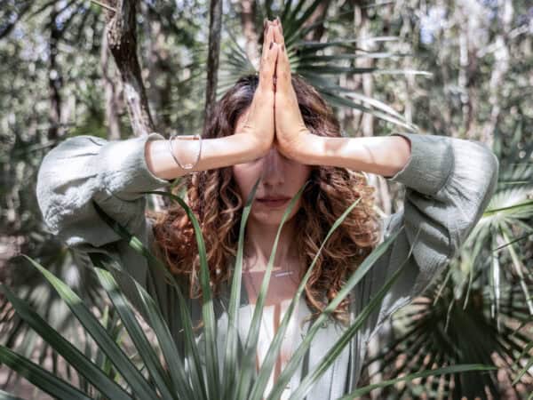 Person im Wald mit gefalteten Händen in Gebetshaltung (Namaste-Geste) als Symbol moderner Spiritualität