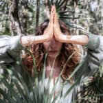 Person im Wald mit gefalteten Händen in Gebetshaltung (Namaste-Geste) als Symbol moderner Spiritualität