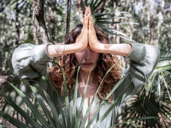 Person im Wald mit gefalteten Händen in Gebetshaltung (Namaste-Geste) als Symbol moderner Spiritualität