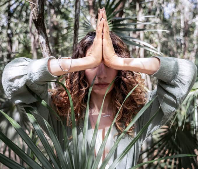Person im Wald mit gefalteten Händen in Gebetshaltung (Namaste-Geste) als Symbol moderner Spiritualität