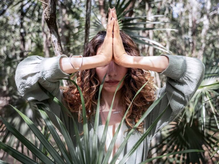 Person im Wald mit gefalteten Händen in Gebetshaltung (Namaste-Geste) als Symbol moderner Spiritualität