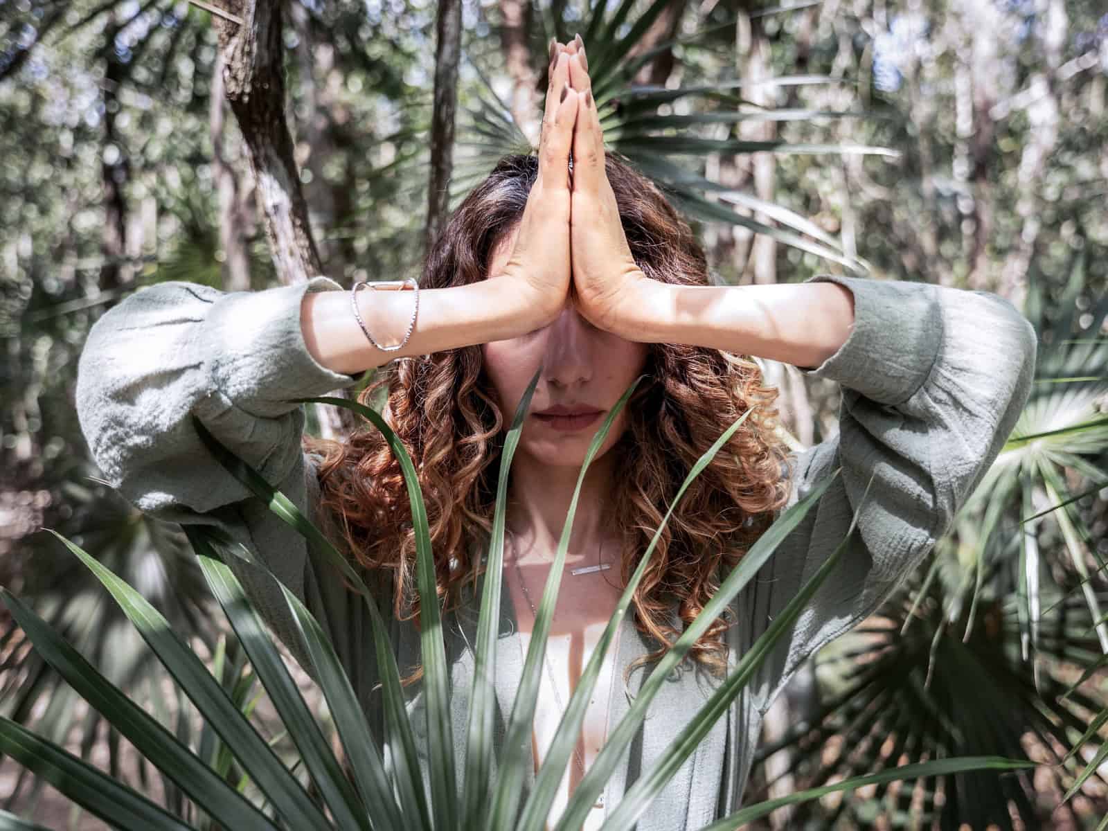 Person im Wald mit gefalteten Händen in Gebetshaltung (Namaste-Geste) als Symbol moderner Spiritualität