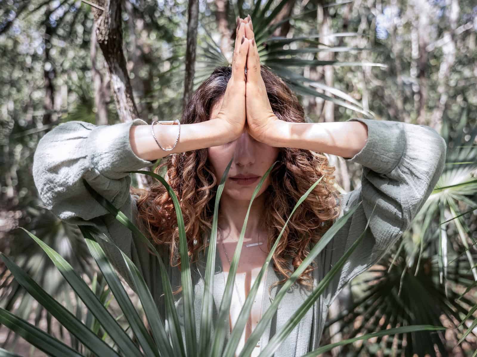 Person im Wald mit gefalteten Händen in Gebetshaltung (Namaste-Geste) als Symbol moderner Spiritualität