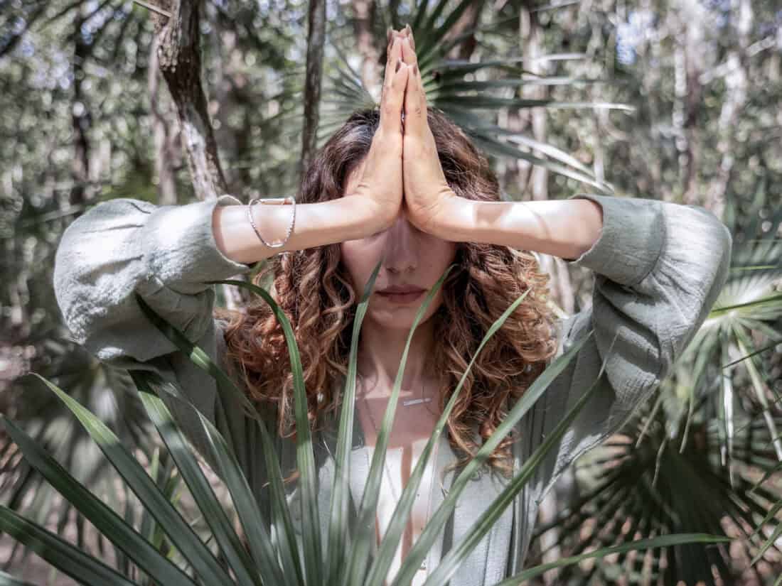 Person im Wald mit gefalteten Händen in Gebetshaltung (Namaste-Geste) als Symbol moderner Spiritualität