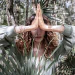 Person im Wald mit gefalteten Händen in Gebetshaltung (Namaste-Geste) als Symbol moderner Spiritualität