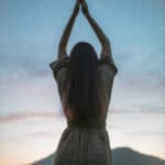 Frau mit erhobenen Armen vor blauem Abendhimmel als Symbolbild für Manifestation und spirituelle Hingabe.
