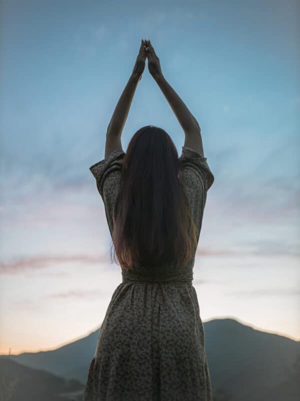 Frau mit erhobenen Armen vor blauem Abendhimmel als Symbolbild für Manifestation und spirituelle Hingabe.