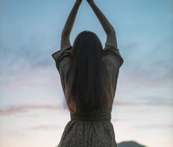 Frau mit erhobenen Armen vor blauem Abendhimmel als Symbolbild für Manifestation und spirituelle Hingabe.