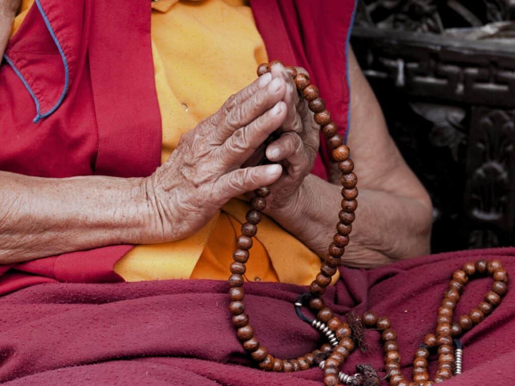 Hände halten eine Mala aus Holzperlen in einem religiösen oder meditativen Kontext.