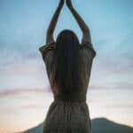 Frau mit erhobenen Armen vor blauem Abendhimmel als Symbolbild für Manifestation und spirituelle Hingabe