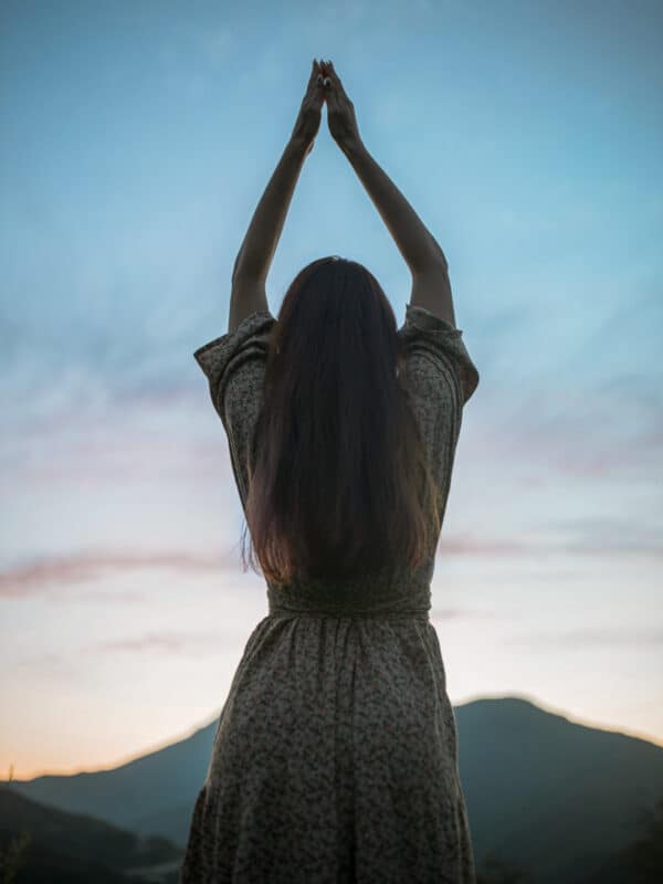 Frau mit erhobenen Armen vor blauem Abendhimmel als Symbolbild für Manifestation und spirituelle Hingabe