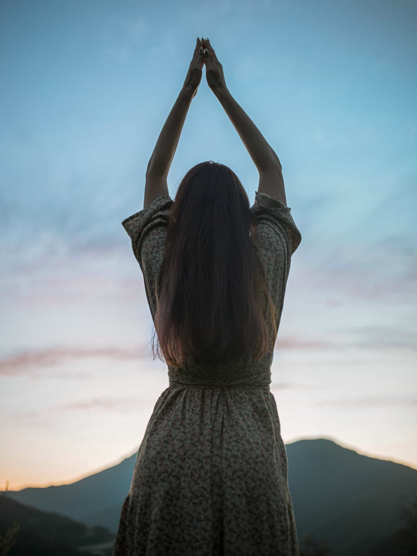 Frau mit erhobenen Armen vor blauem Abendhimmel als Symbolbild für Manifestation und spirituelle Hingabe