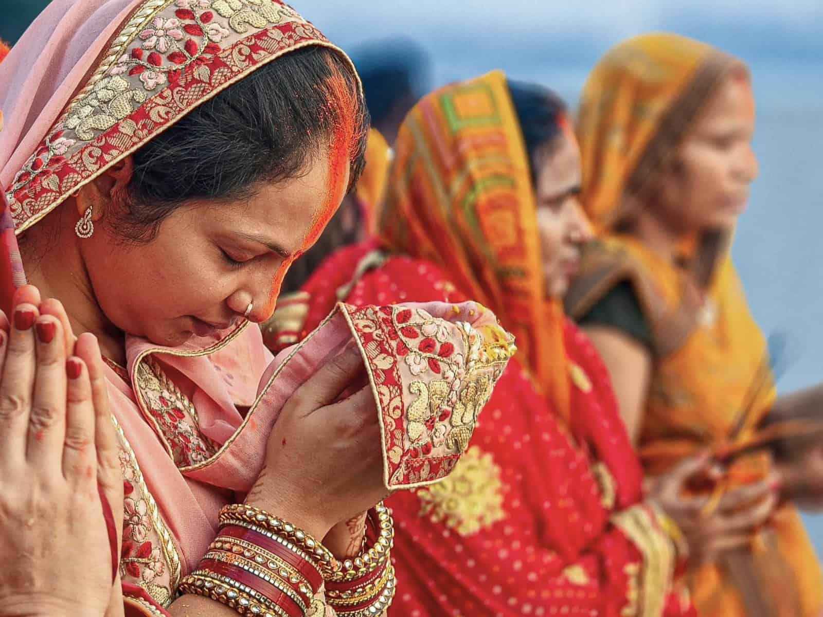 Mehrere Frauen in traditioneller Kleidung stehen nebeneinander und halten die Hände vor der Brust im Namaste-Gruß. Bild zur Gegenüberstellung von kultureller Aneignung in der modernen Spiritualität.