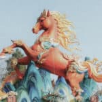 Große rot-orange Pferdefigur - das chinesische Feuerpferd - mit flammenförmiger Mähne vor hellem Himmel, Teil einer chinesisch wirkenden Dekoration.