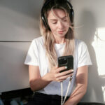 Junge Frau mit Kopfhörern schaut auf ihr Smartphone und nutzt ChatGPT möglicherweise für ein Coaching.