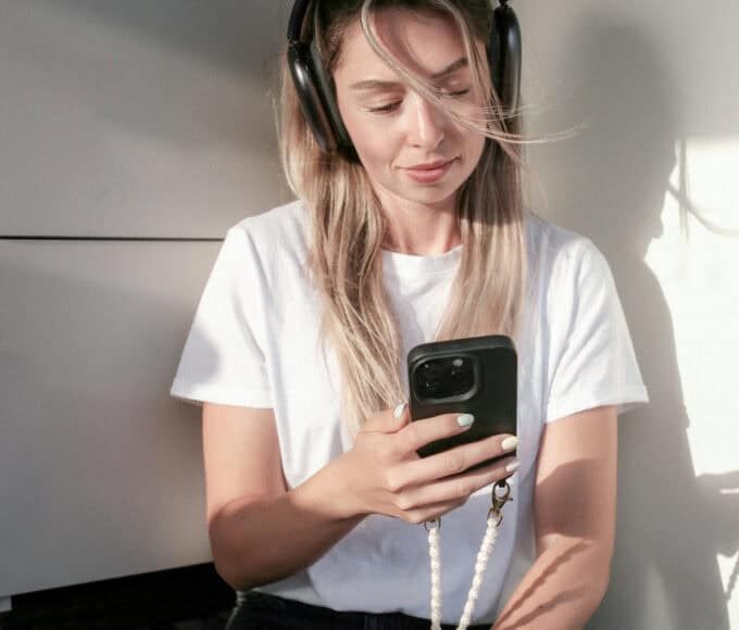 Junge Frau mit Kopfhörern schaut auf ihr Smartphone und nutzt ChatGPT möglicherweise für ein Coaching.